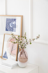 Wall Mural - Vase with blossoming branches and pictures on shelf near light wall