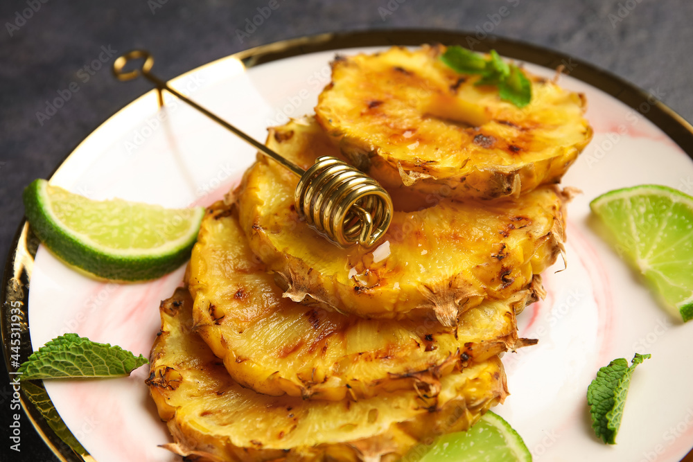 Plate with grilled pineapple slices, honey and lime on dark background, closeup