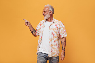 white haired man in plant shirt pointing to place for text on orange background. adult in white t-sh