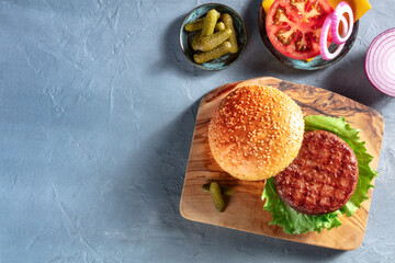 Burger ingredients. Hamburger patty, sesame bun,m tomato, onion and pickles, shot from the top on a blue background with copy space. Hamburger recipe