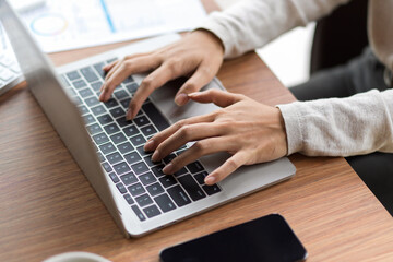 Typing on laptop keyboard with mobile phone and financial papers on the wooden desk