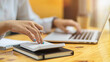 © bongkarn - Close up of female accountant fingers using calculator and typing on laptop