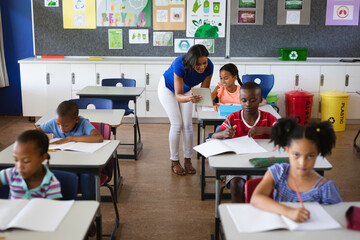 Wall Mural - African american female teacher with digital tablet teaching a girl at elementary school