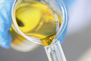 Wall Mural - Scientist chemist pouring yellow oil from glass jar into test tube closeup