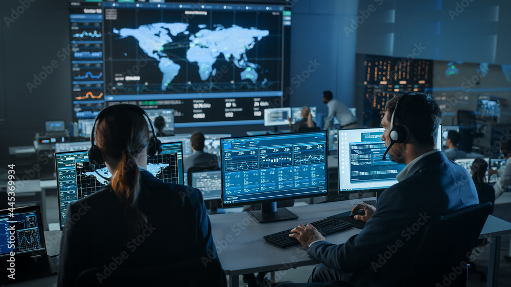 Shot of Officers in a Surveillance Control Center with Police Global Map Tracking on a Big Digital Screen. Monitoring Room Employees Sit in Front of Computer Displays and Analyze Big Data. - obrazy, fototapety, plakaty 