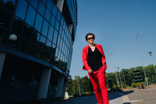 A Girl In A Red Suit Stands Against The Background Of A Modern Building In The City