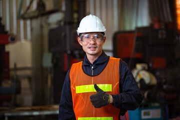 Wall Mural - Portrait of Asian male worker in protection glasses and helmet smile showing thumbs up in front of industry machine at industrial factory. quality control guarantee with copy space