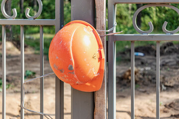 Wall Mural - A working construction helmet hangs on the fence. Completion concept. Builders protest about low wages. Builders Union - Compliance with Workers' Requirements.