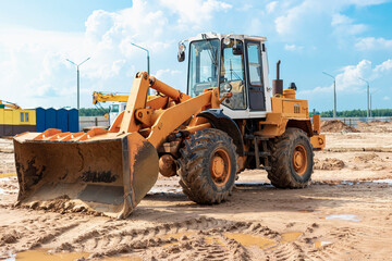 Heavy wheel loader with a bucket at a construction site. Equipment for earthworks, transportation and loading of bulk materials - earth, sand, crushed stone.