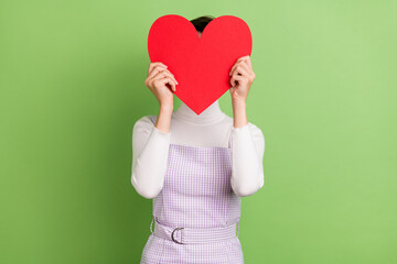 Poster - Photo of young girl close cover face big red paper heart card anonym incognito isolated over green color background