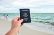 One single hand holding a blue American passport while on vacation at the beach 