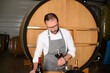 © W PRODUCTION - Portrait of a mature man oneologist tasting wine bottle in wine cellar with wooden barrel