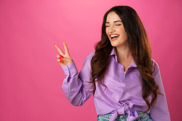 Wall Mural - Happy smiling woman showing victory sign against pink background