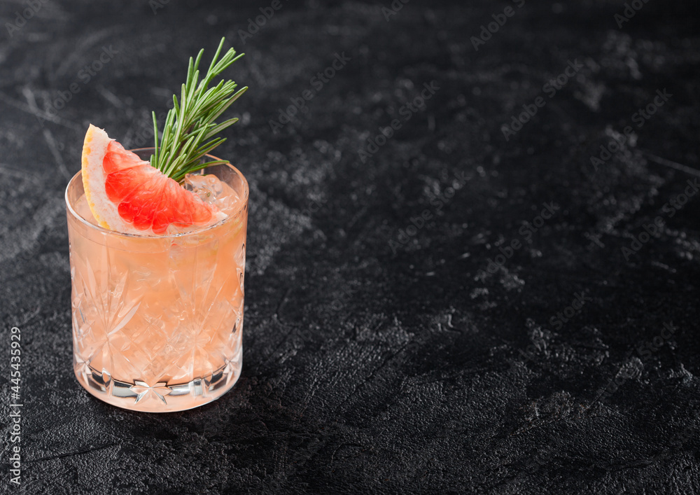 Grapefruit and rosemary drink, alcohol or non-alcohol cocktail in glass with ice cubes on black background. - obrazy, fototapety, plakaty 