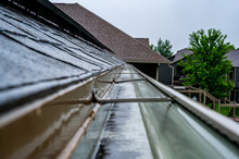 Selective Focus On A Section Of Residential Guttering With Hanger Conveying Water During A Storm. Rain Splatters And Drops Visible.