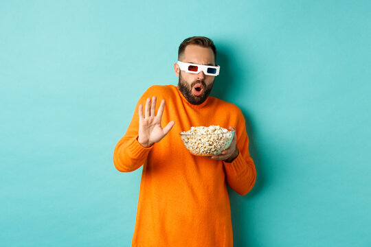Image of man in 3d glasses watching movie, getting scared of special effects, looking in awe, standing with popcorn against white background