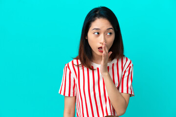 Wall Mural - Young Vietnamese woman isolated on blue background whispering something with surprise gesture while looking to the side