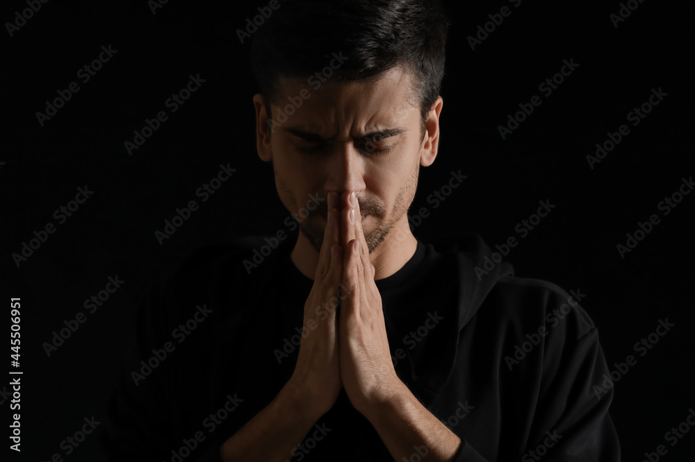 Religious young man praying on dark background - obrazy, fototapety, plakaty 