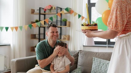 Wall Mural - family, holidays and people concept - portrait of happy mother, father and little son with firework candle burning on birthday cake sitting on sofa at home party