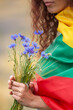 Woman covered with flag of Lithuania holding bouquet of blue cornflowers in a rye field. Vertical image. Independence restoration Day. King mindaugas day. Love Lithuania concept. Selective focus.