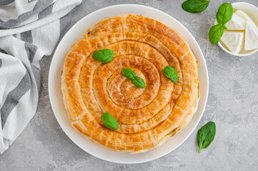 Wall Mural - Greek pie spanakopita with feta cheese and spinach on a white plate on a gray concrete background. Copy space.