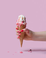 A Female Hand Holds An Ice Cream Cone With Cherry Jam In A Waffle Glass On A Pink Background. Ice Cream Melted And Flowed Over Fingers
