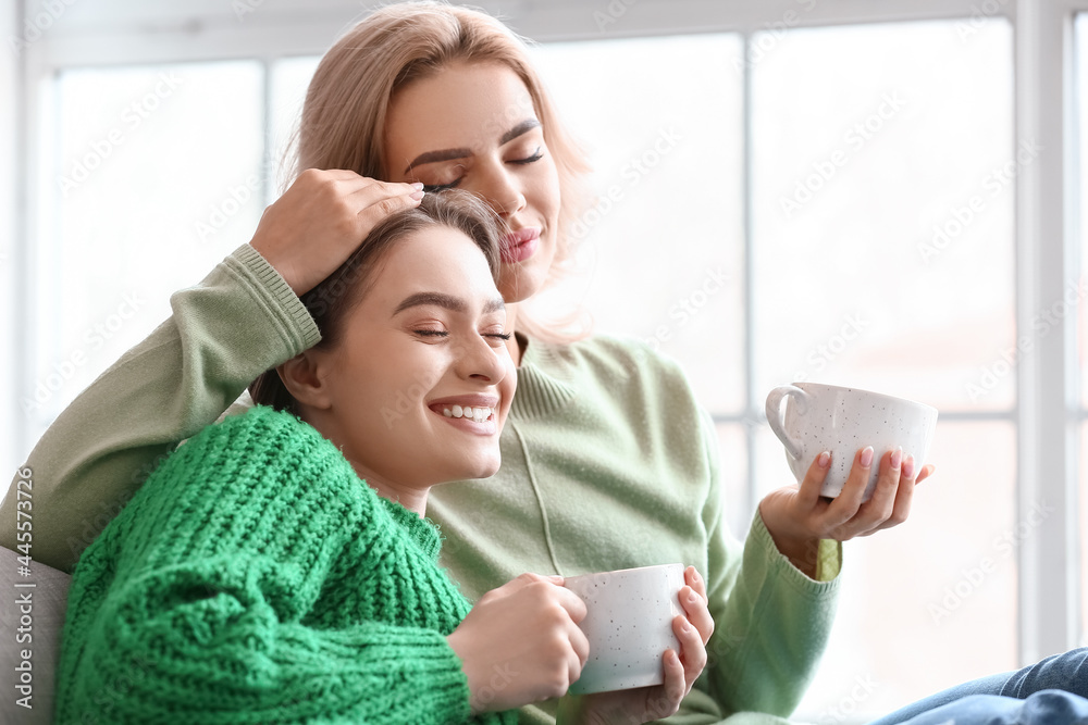 Beautiful young sisters drinking tea at home