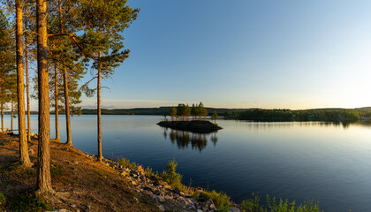 Wall Mural - Panorama of a calm lake with small island and golden sunset evening light on the trees and forest on the lakeshore in the foreground