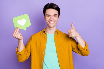 Sticker - Photo of nice brunet young guy hold heart show thumb up wear yellow shirt isolated on violet color background