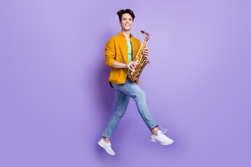 Poster - Full body profile side photo of young man happy positive smile jump up play saxophone isolated over violet color background