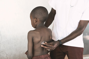 African ethnicity black male doctor checking respiratory health conditions of a little African boy with his stethoscope.