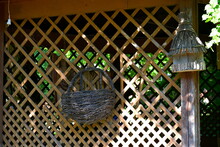 A Close Up On A Straw Or Wicker Basked Attached To A Wooden Fence Or Wall With A Small Bird Feeding Shack Located Nearby Spotted In The Middle Of A Rural Polish Village On A Sunny Summer Day