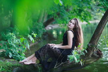 a beautiful young cheerful girl with long flowing hair in a black long dress laughs and sits on a cu