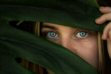 Closeup Shot Of A Woman With Blue Eyes Hiding Behind Leaves
