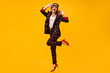 © Look! - Beautiful lady in stylish suit, cap and eyeglasses jumping on orange background. Happy woman in modern outfit and red shoes posing..