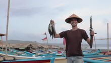 Happy Young Fisherman On The Beach Holding His Catch Fish And Shows In Front Of His Boat