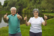 © Studio Romantic - Cheerful energetic senior people enjoying sports exercise. Portrait of happy old couple standing in green park, looking at camera, smiling and giving thumbs up. Fitness and healthy lifestyle concept