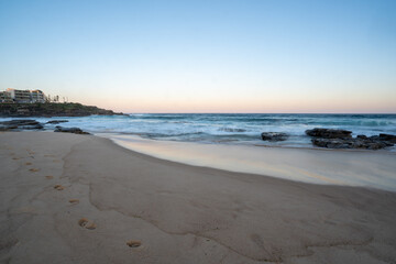 Wall Mural - Sunset at the beach with footprints in the sand and slow motion waves