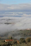 Fototapeta Natura - The green rolling hills of Umbria, Italy, a quaint maroon roofed country house in the foreground, submerged in towering thick grey, blue and white clouds, on a late autumn morning