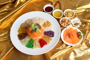 chinese new year colourful lo hei yu sheng with smoked salmon, vegetables and sauces in white gold background asian halal menu for cny festival