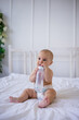a baby girl in a diaper holds a bottle of water and sits on a white bed