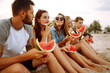 © maxbelchenko - Young friends relaxing on the beach and eating watermelon. Group of young sitting together sitting near the sea and  enjoy summer party. People, lifestyle, travel, nature and vacations concept.
