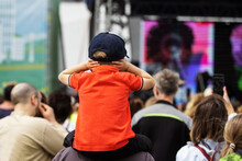 A child at a street concert covers his ears due to loud music. Unrecognizable person. Back view