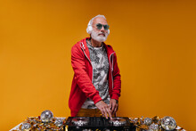 Man In Red Jacket And Headphones Makes Music With Dj Controller. Adult Guy With Grey Hair In Stylish Sweatshirt And Blue Sunglasses Posing..