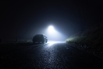 Wall Mural - A lone car, parked on the side of the road, underneath a street light, on a spooky, scary, rural, country road. On a foggy winters night