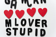 loosely arranged black chalk letters with affectionate message lover stupid and hand painted red hearts on white background