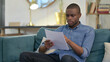 © stockbakers - Young African Man Reading Documents on Sofa