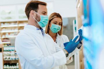 Wall Mural - Male and female pharmacists with protective mask on their faces working at pharmacy. Medical healthcare concept.