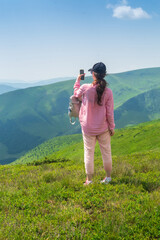 Wall Mural - A tourist is relaxing in nature and uses the Internet on a smartphone. The girl traveler photographs a panorama of the mountains on a mobile phone. Mountain beautiful landscape