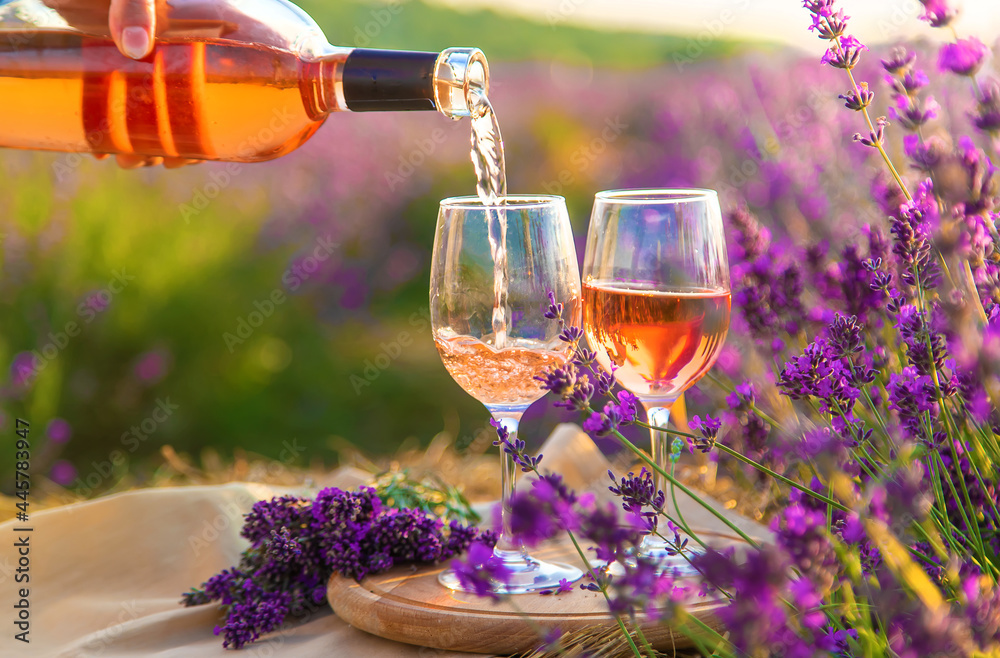 A woman holds wine in glasses. Picnic in the lavender field. Selective focus. - obrazy, fototapety, plakaty 